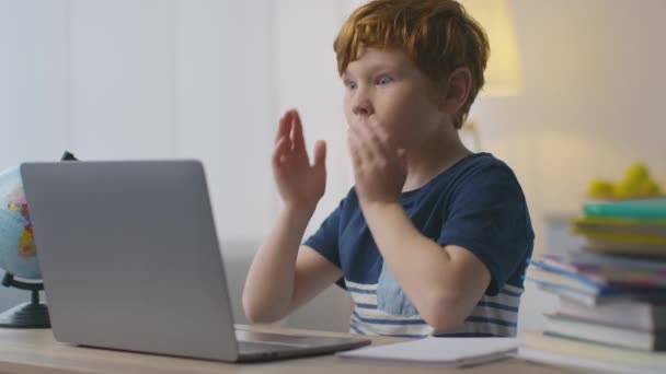 Retrato del niño pelirrojo sorprendido mirando al portátil con expresión asombrada, tocándose las mejillas con asombro - Imágenes, Vídeo
