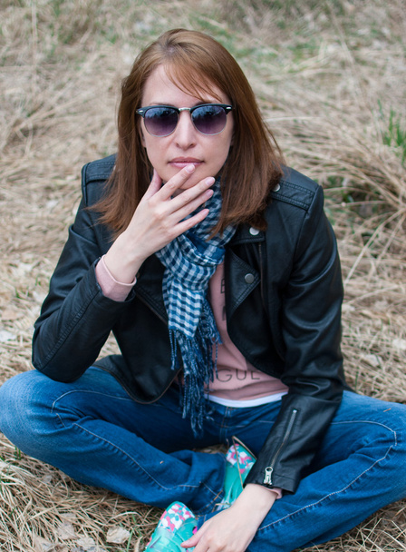 Young woman in a black jacket and jeans sitting on the hay - Photo, Image