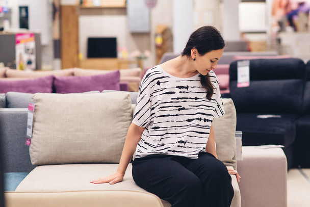 Customer woman buying new furniture. Woman checking quality of sofa in a store. Furniture shop. Young woman choosing new furniture for her new modern home. Furnishings store. - Foto, Imagem