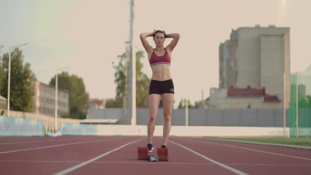 Caucasian young brunette woman shit for a run in the stadium comes up to the running sides and starts the sprint race in slow motion - Filmmaterial, Video