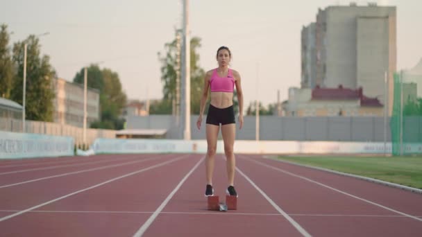 Een jonge vrouw renner in het zonlicht in het stadion arena klaar voor de run krijgt in loopschoenen en loopt sprint vanaf de startlijn in slow motion - Video