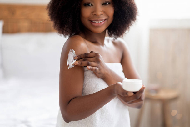 Jolie jeune femme afro appliquant de la crème sur le corps, se dorloter après le bain ou la douche à la maison - Photo, image