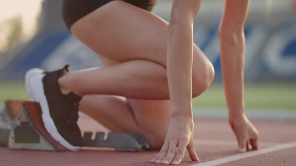Μια νεαρή γυναίκα τρέχει στο φως του ήλιου στην αρένα του σταδίου ετοιμάζεται για το τρέξιμο παίρνει σε αθλητικά παπούτσια και τρέχει σπριντ από τη γραμμή εκκίνησης σε αργή κίνηση - Πλάνα, βίντεο