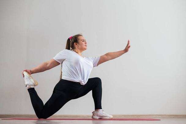 Young fat woman doing flexibility exercises on a white background - Foto, imagen