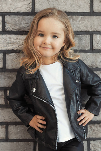 Close-up portrait cute pretty girl 2-3 years old in fashion outfit: white t-shirt, leather black jacket and leggings.  - Фото, зображення