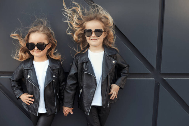 Two sisters in same outfits: white t-shirts, leather black jackets and leggings, sunglasses hearts. - Foto, Bild