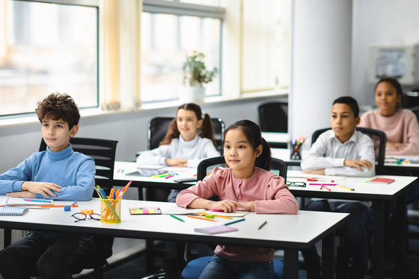 Portrait of focused diverse pupils sitting at desk in classroom - 写真・画像