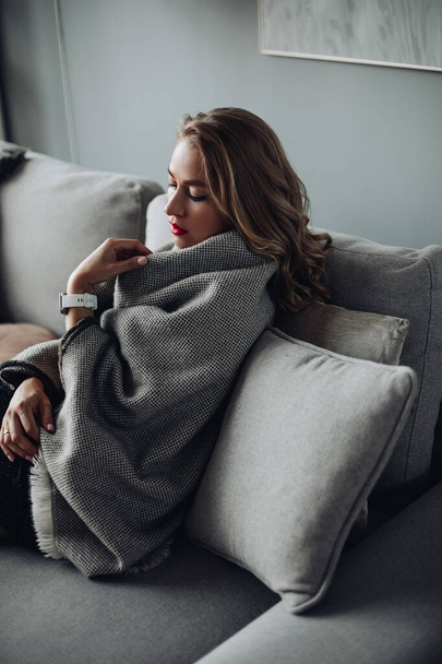 atractiva mujer con el pelo claro se encuentra en un sofá con una cubierta caliente - Foto, Imagen