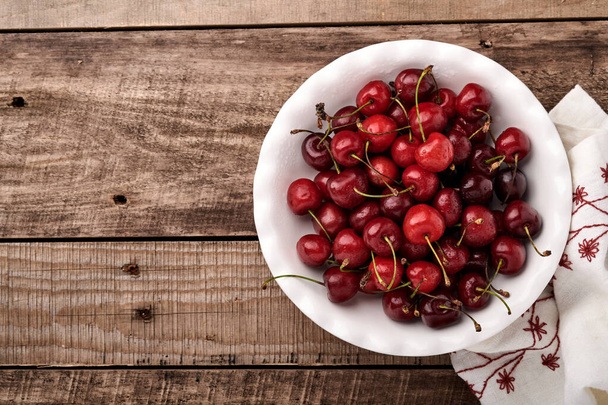 Cherry with water drops on white bowl on dark brown stone table. Fresh ripe cherries. Sweet red cherries. Top view. Rustic style. Fruit Background - Photo, image