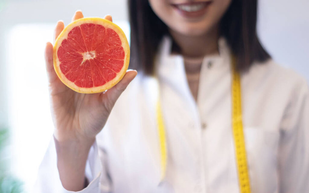 female nutritionist in apron and tape measure holding grapefruit  - Photo, Image
