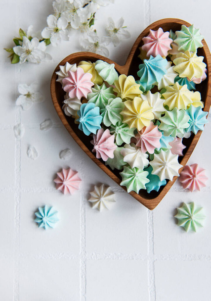 Pequeños merengues coloridos en el tazón en forma de corazón de madera sobre fondo de baldosa blanca - Foto, Imagen