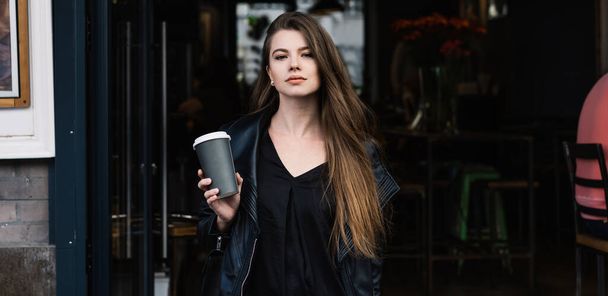 Beautiful stylish female with plactic cup of fresh coffee standing near modern cafe and looking at camera on street on daytime - Fotoğraf, Görsel