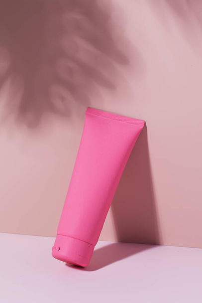 A pink tube with a cosmetic product on a pink background with a shadow from a leaf. Mockup cream for face and body. - Φωτογραφία, εικόνα