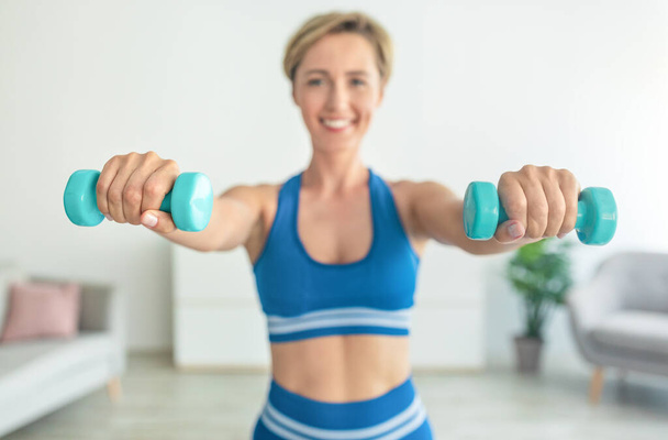 Smiling Middle-Aged Woman Exercising With Two Dumbbells - Foto, afbeelding