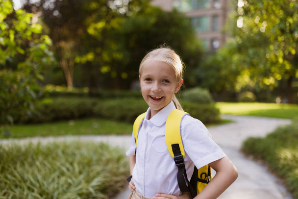 Back to school. Little girl with yellow backpack from elementary school outdoor. Kid going learn new things 1th september after end Coronavirus covid-19 quarantine and self isolation  - Foto, Imagen