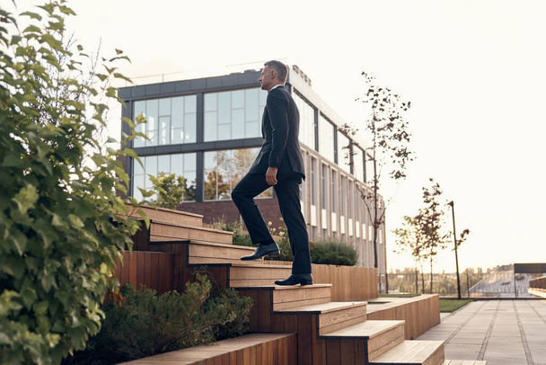 Confident mature man in full suit walking up by staircase outdoors - Valokuva, kuva