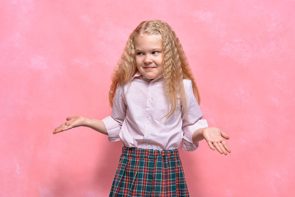little girl shows emotion. surprised schoolgirl in uniform. pink background - 写真・画像