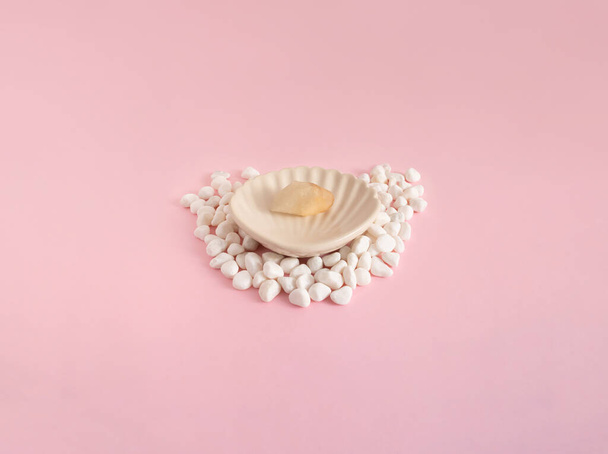 Un coquillage avec un rocher de perles entouré de petites roches blanches, sur un fond rose pâle - Photo, image
