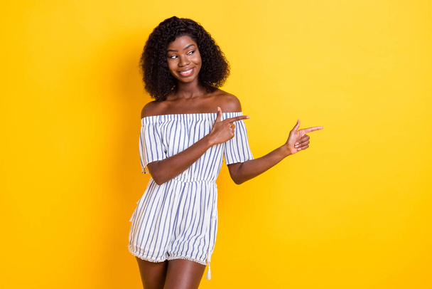 Photo of cute sweet dark skin woman wear striped outfit looking pointing fingers empty space isolated yellow color background - Foto, Imagen