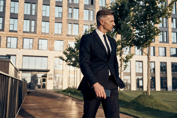Confident mature businessman walking outdoors with office building on the background - Фото, зображення