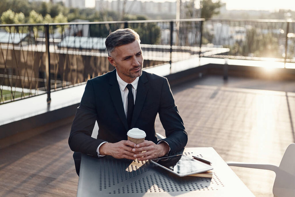 Confident mature man in formalwear enjoying coffee while sitting in cafe outdoors - Photo, Image