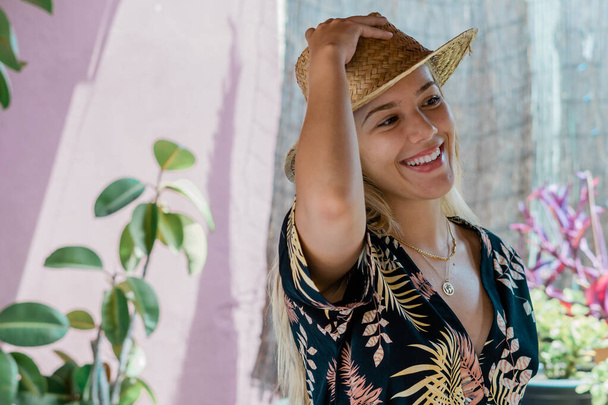Smiling and happy young blonde woman putting on a hat - Foto, imagen