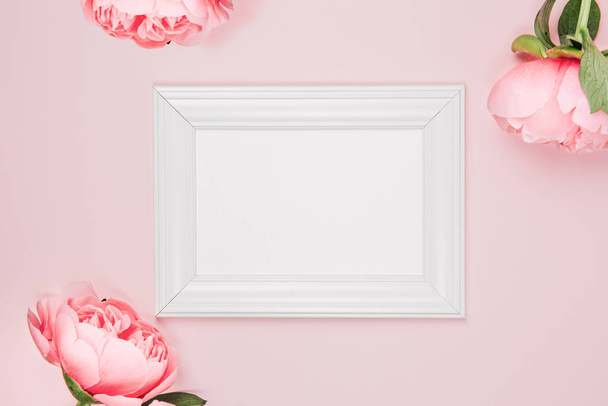 Mockup photo frame on a pink background with flowers. Delicate elegant background with pink peonies, peony buds. Flat lay, top view - Фото, изображение