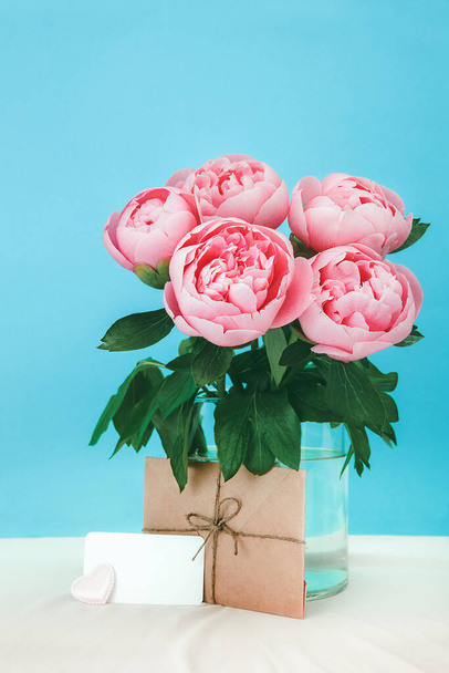 Kaunis vaaleanpunainen pioni kukkia kukkakimppu lasi maljakko syaani taustalla. Pisaroita vettä terälehti pioneja - Valokuva, kuva