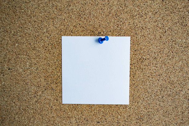 A white paper note on a cork board, attached with a blue pushpin. Copy space. - Photo, Image