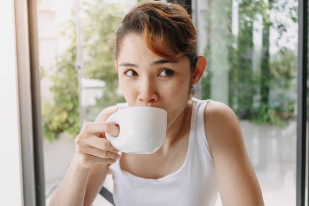 Woman in white tank top is drinking hot drink in the cup. - Fotoğraf, Görsel