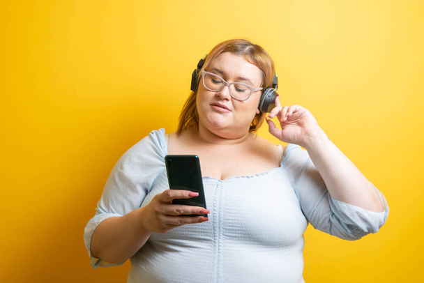 Fiatal plusz méret kaukázusi modell zenét hallgat fejhallgatóval a mobiljáról - Fotó, kép