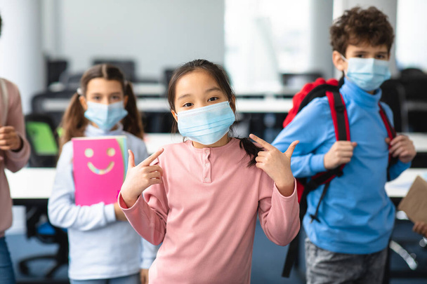 Asian girl pointing at her face mask standing in classroom - Photo, image