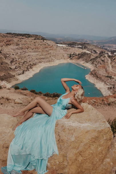fashion outdoor photo of beautiful woman with blond hair in elegant dress posing on the hill with lake view - Foto, imagen