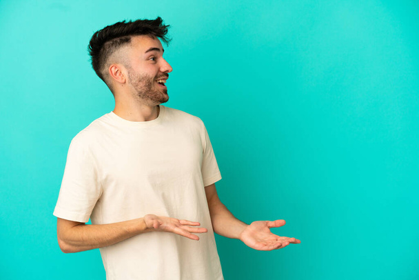 Young caucasian man isolated on blue background with surprise expression while looking side - Fotografie, Obrázek