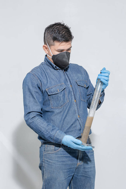 Travailleur industriel avec masque protecteur et gants en latex bleu tenant une grande pipette pour effectuer un test géologique en laboratoire - Photo, image