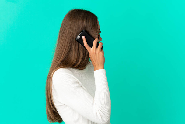 Giovane donna su sfondo blu isolato mantenendo una conversazione con il telefono cellulare con qualcuno - Foto, immagini