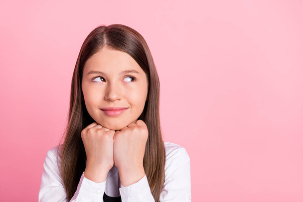 Photo of young school girl happy positive smile hands touch chin think dream look empty space isolated over pink color background - Фото, изображение