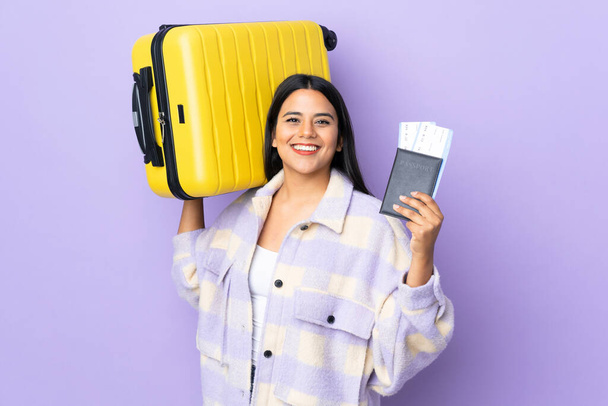 Mladá latinská žena žena izolované na fialovém pozadí v dovolené s kufrem a pasem - Fotografie, Obrázek