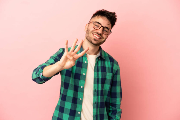 Jeune homme caucasien isolé sur fond rose heureux et comptant quatre avec les doigts - Photo, image