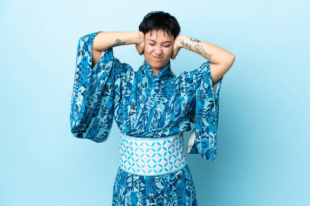 Giovane donna che indossa kimono su isolato sfondo blu frustrato e coprendo le orecchie - Foto, immagini