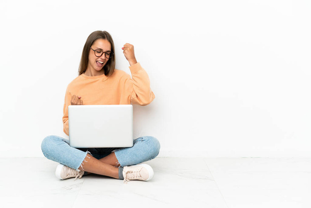 Dizüstü bilgisayarı olan genç bir kadın yerde oturmuş zaferi kutluyor. - Fotoğraf, Görsel