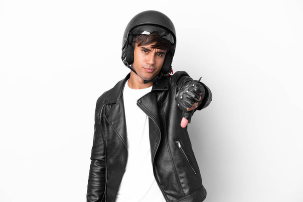 Jongeman met een motorhelm geïsoleerd op witte achtergrond met duim naar beneden met negatieve expressie - Foto, afbeelding