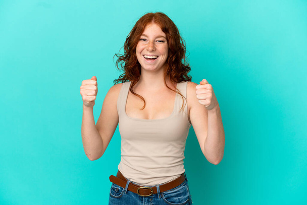 Teenager rötliche Frau isoliert auf blauem Hintergrund feiert einen Sieg in der Siegerposition - Foto, Bild