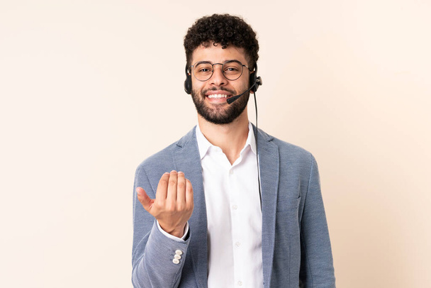 Telemarketer Moroccan man working with a headset isolated on beige background inviting to come with hand. Happy that you came - Foto, afbeelding