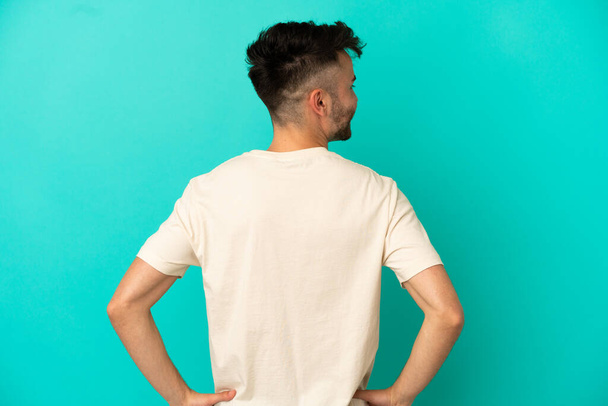 Young caucasian man isolated on blue background in back position and looking side - Fotoğraf, Görsel