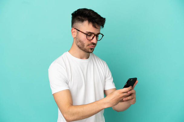 Fiatal fehér férfi elszigetelt kék háttér küld egy üzenetet vagy e-mailt a mobil - Fotó, kép