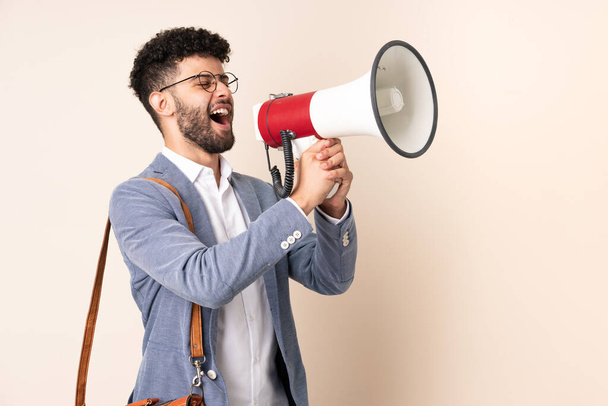 Young business Moroccan man isolated on beige background shouting through a megaphone - Foto, afbeelding