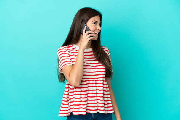Young Brazilian woman isolated on blue background keeping a conversation with the mobile phone with someone - Photo, Image