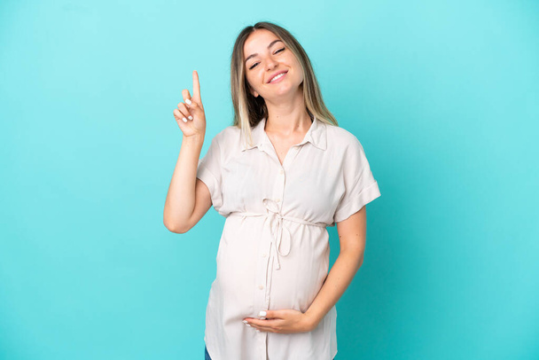 Giovane donna rumena isolata su sfondo blu incinta e rivolta verso l'alto - Foto, immagini