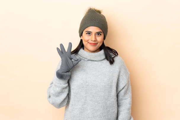 Menina colombiana jovem com chapéu de inverno isolado no fundo bege mostrando um sinal ok com os dedos - Foto, Imagem
